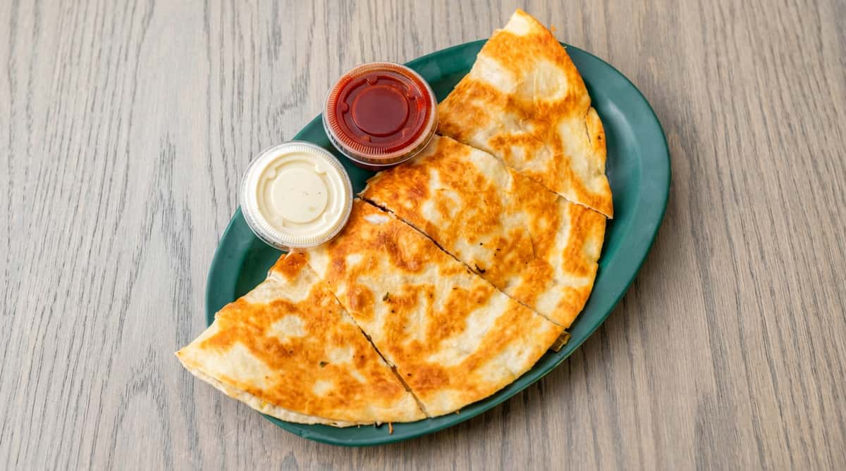 Quesadilla cut into wedges on a green plate, with small containers of red sauce and sour cream.