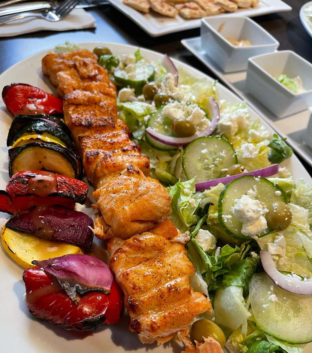 Grilled salmon and vegetable skewers served with a fresh Greek salad featuring cucumbers, olives, feta cheese, and red onions.