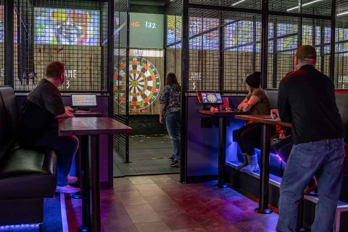A group of young professionals in casual dress enjoying axe throwing and laughing with drinks in hand at Block Party Social.
