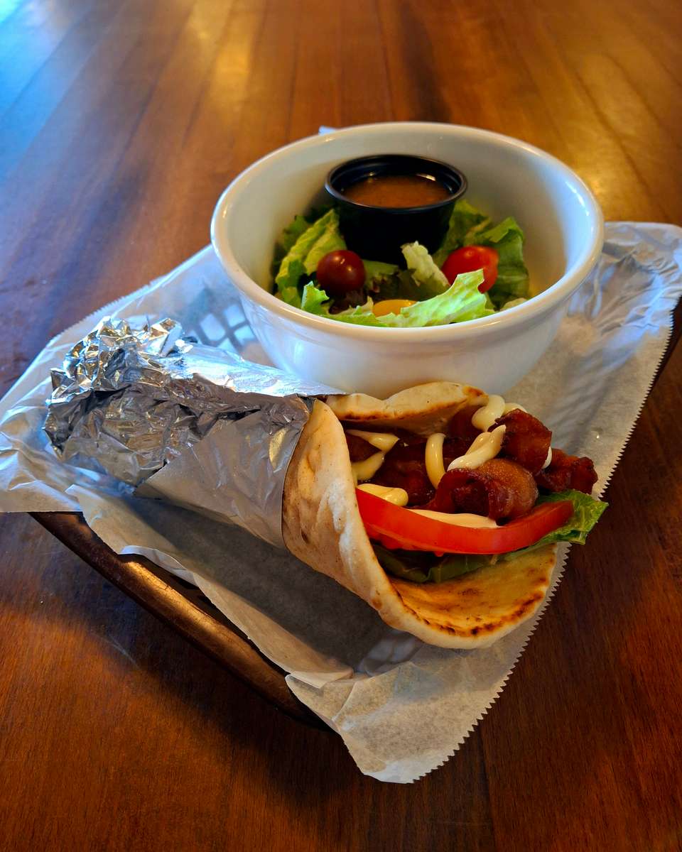 Grilled meat wrap with lettuce and tomato served alongside a fresh salad and dressing.