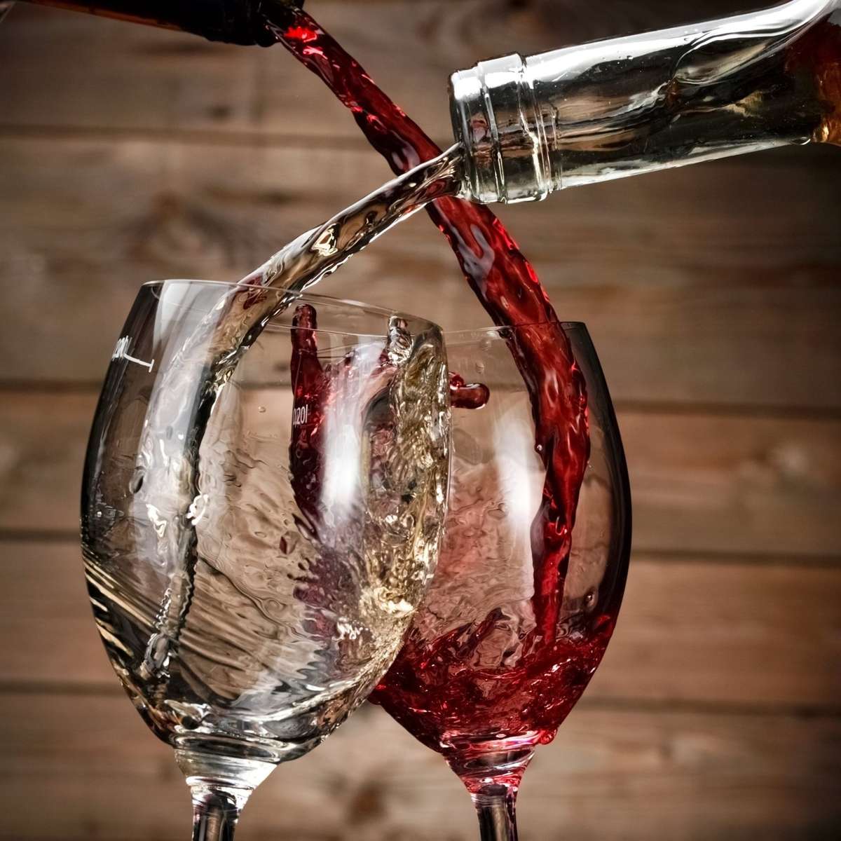 Red and white wine being poured simultaneously into two crossing glasses.