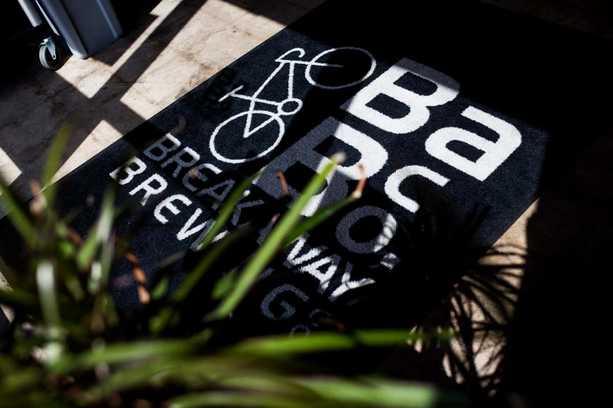 Sunlight casts shadows over a black mat featuring a white bicycle graphic and the words "Breakaway Brewing Co." partially visible.