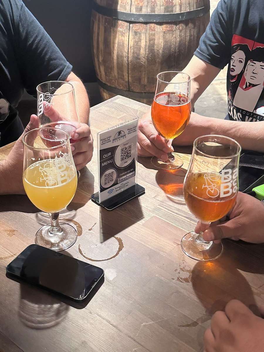 Friends toasting with glasses of craft beer in a warmly lit bar, with a woman smiling in the background.