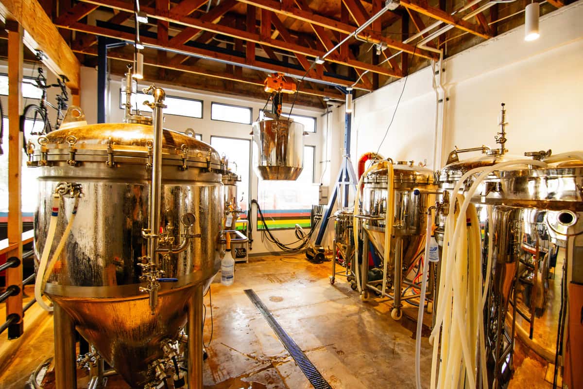 Stainless steel brewing tanks in a craft brewery with exposed beams and industrial piping.