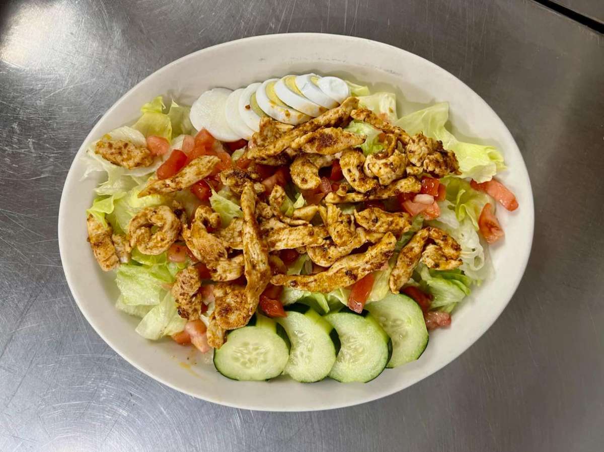 Grilled chicken salad with lettuce, diced tomatoes, cucumber slices, and sliced boiled egg served in an oval bowl.