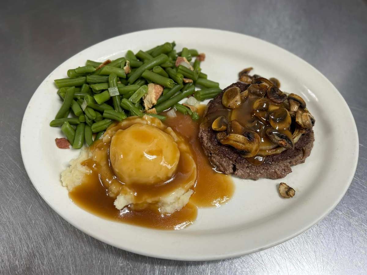 Salisbury steak topped with mushroom gravy, served with mashed potatoes and green beans with bacon.