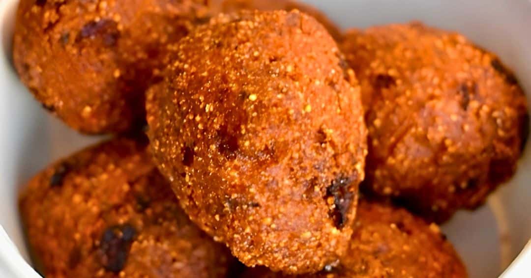 A close-up shot of several golden-brown, deep-fried Sweet Onion Hush Puppies resting in a white bowl. The exterior of the hush puppies is crispy and highly textured, showing the coarse grains of the cornmeal batter and darker caramelized spots from the sweet onion.