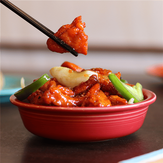 sweet and sour chicken with vegetables in a bowl being eaten with chopsticks