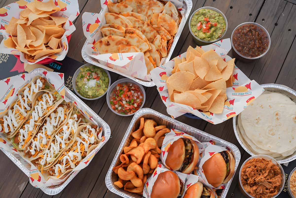 Assorted Mexican dishes including tacos, quesadillas, chips, dips, and sliders arranged on a dining table