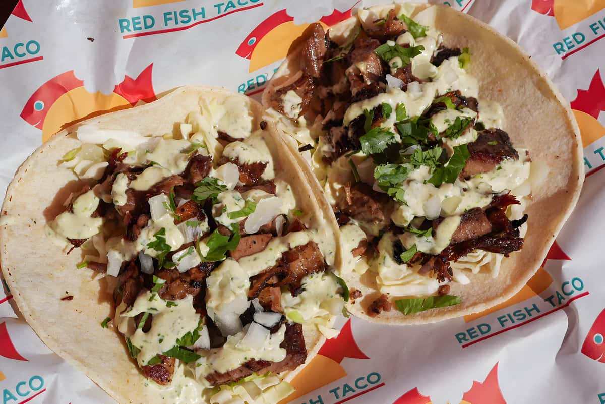 Street style tacos topped with seasoned meat, onions, cilantro, and creamy sauce on flour tortillas.