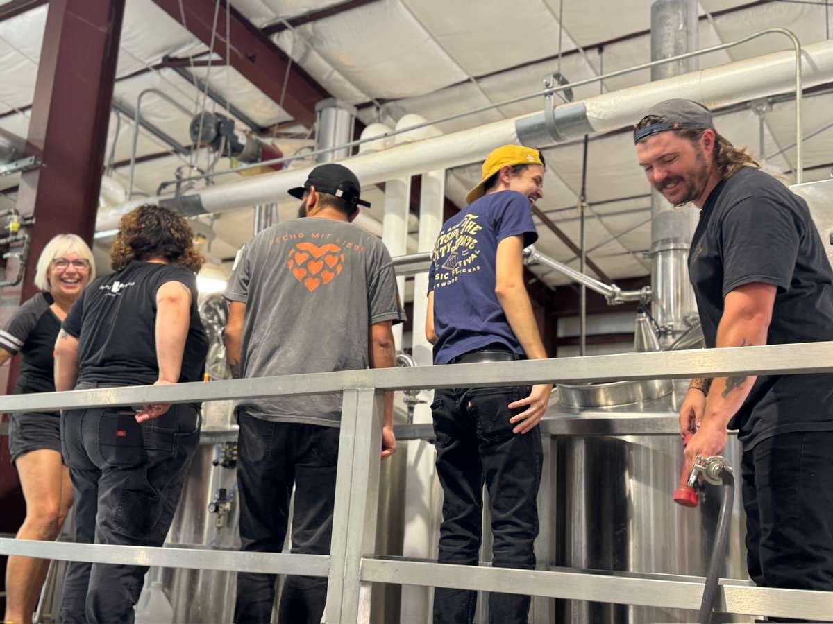 Brew team at Künstler Brewing smiling and working together around stainless steel tanks in the brewery, showcasing a collaborative craft beer production environment.