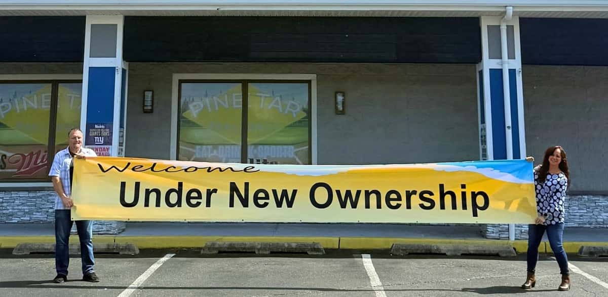 Rick and Dawn holding "Under New Ownership" banner