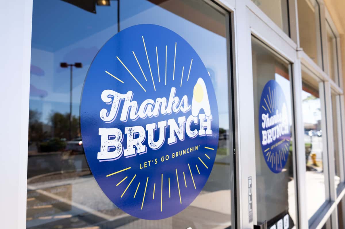 A glass storefront window with a blue "Thanks Brunch" decal and customers dining inside.