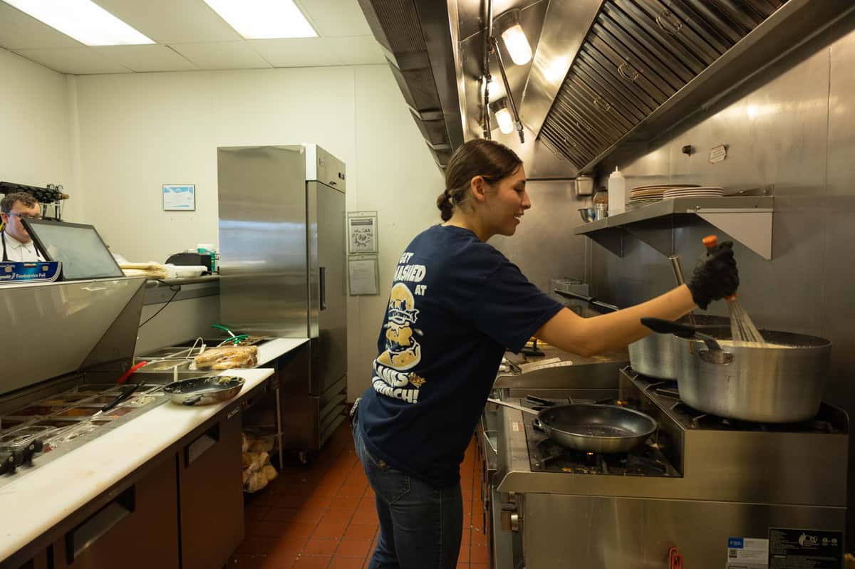 A kitchen staff member working at a stainless steel prep station.