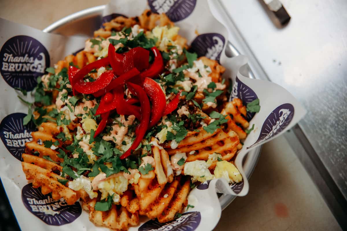 A bowl of waffle fries topped with cheese, peppers, and herbs.