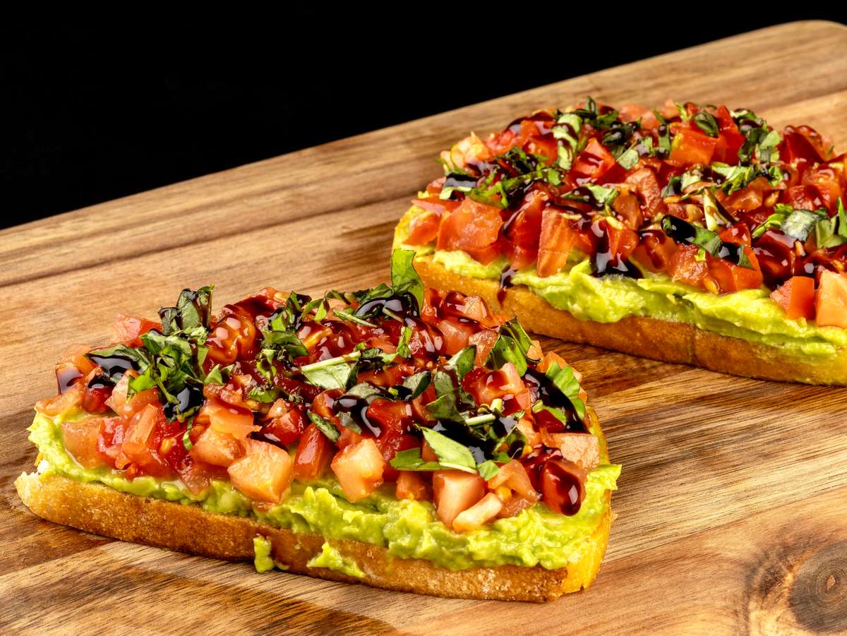 Two slices of toast topped with mashed avocado, tomatoes, and balsamic glaze.