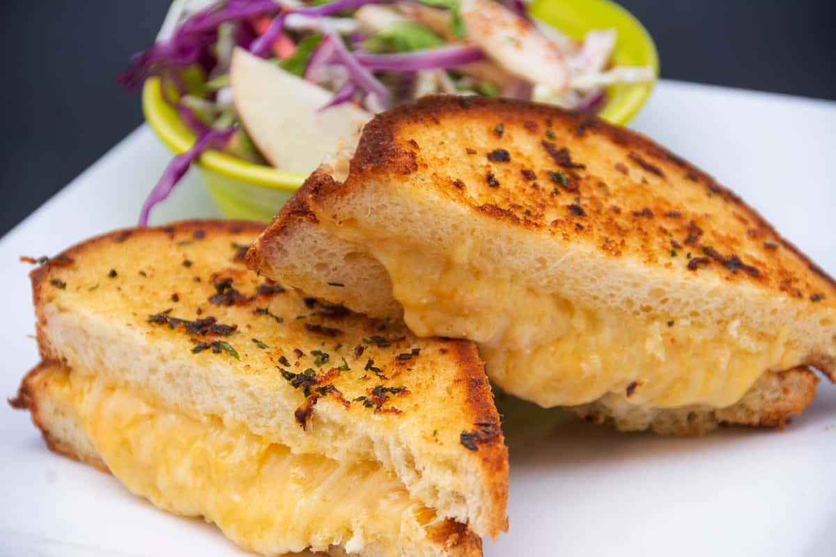 Buttery grilled cheese sandwich with melted cheddar on toasted bread, served with apple cabbage slaw in a lime green bowl.