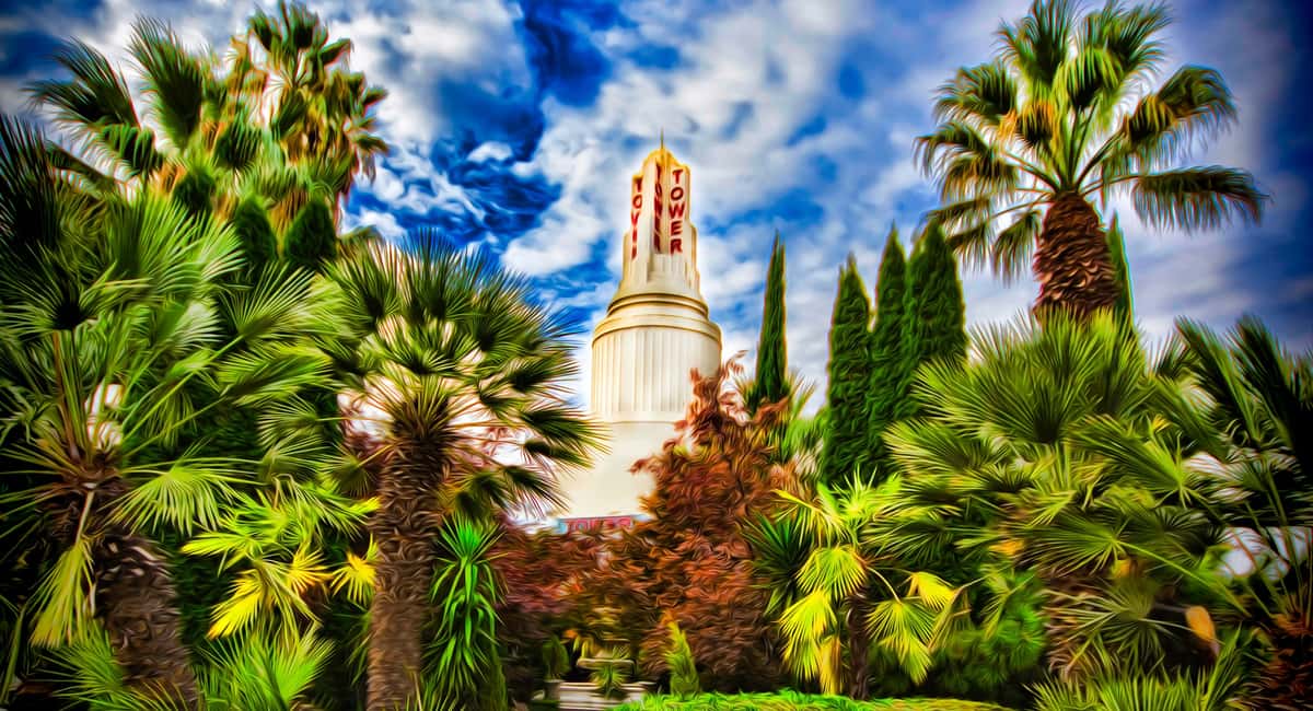 Vibrant view of the Tower Theatre framed by lush palm trees and greenery under a dramatic, cloud-filled sky.