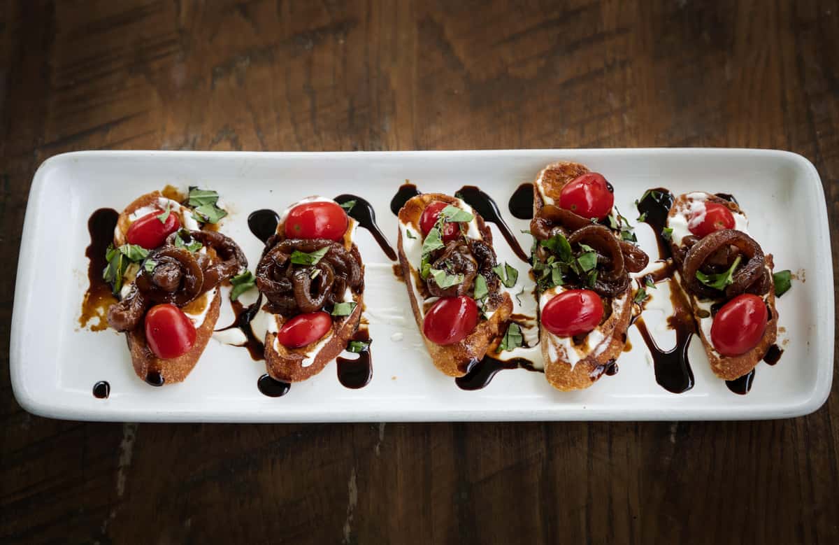 Whipped Goat Cheese Bruschetta with caramelized onions, grape tomatoes, fresh basil and a balsamic reduction drizzle.