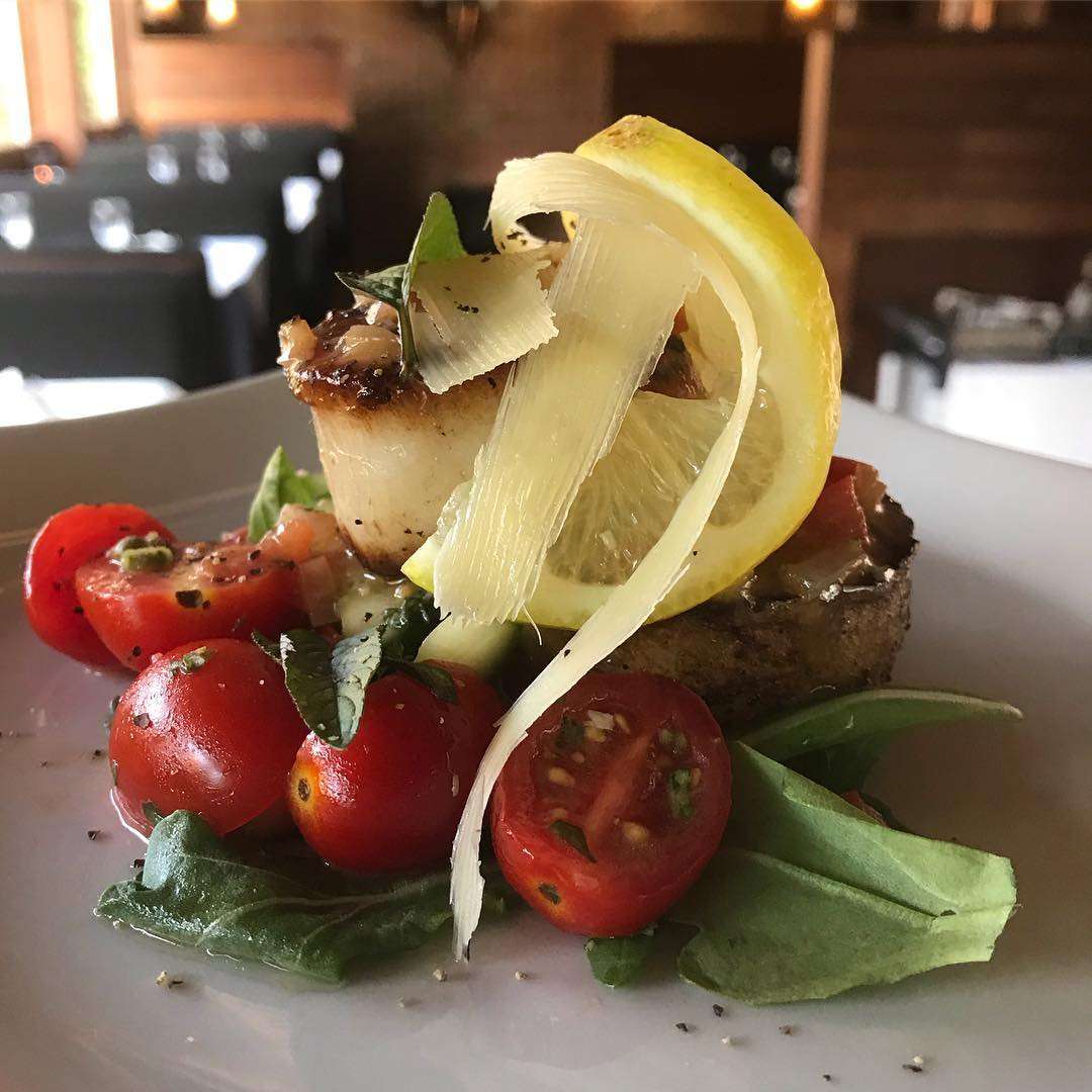 seared scallop on a roasted potato medallion with tomatoes, cucumbers, and fresh basil, dressed with a honey shallot vinaigrette and topped with shaved Parmesan