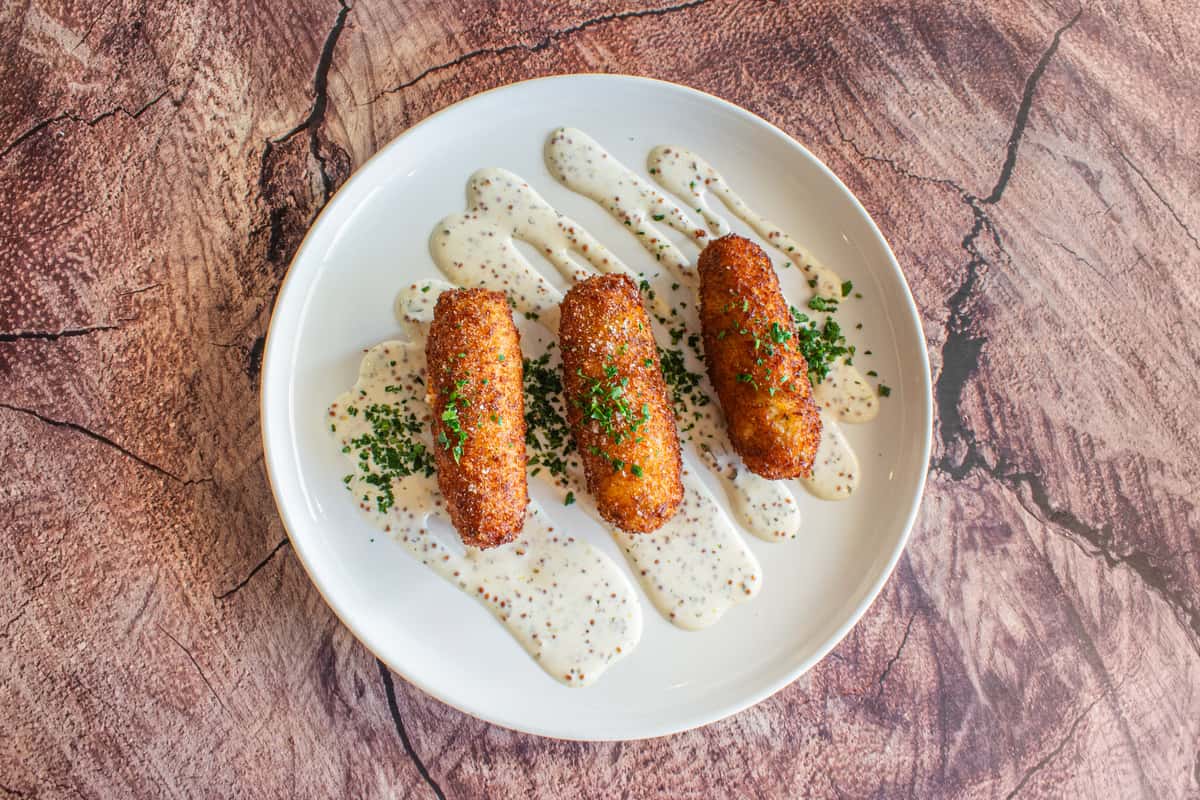 Golden-brown salmon croquettes served over a creamy sauce and garnished with fresh herbs. Crispy on the outside and tender inside, this beautifully plated seafood entrée offers a delicious balance of rich flavor and elegant presentation.