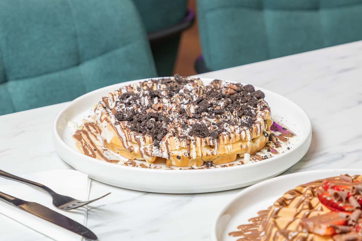 waffle topped with chocolate sauce, white chocolate sauce, oreo crumbs, and chocolate flakes