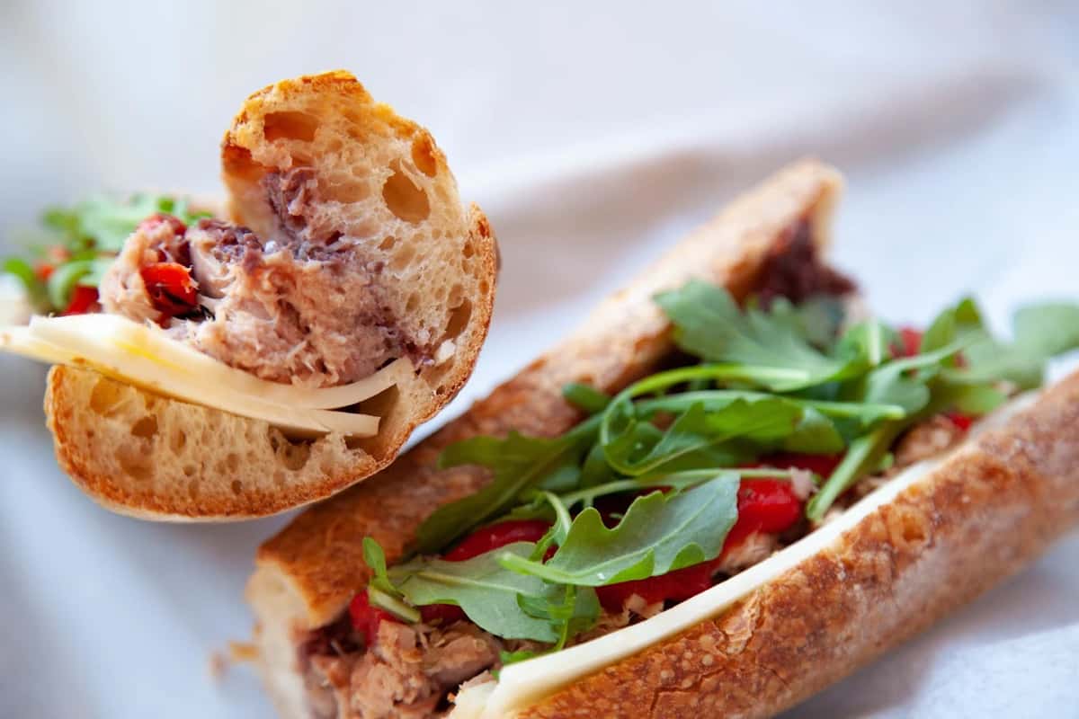 Rustic Italian tuna sandwich with arugula, roasted red peppers, and sharp provolone on crusty bread, styled on parchment paper.