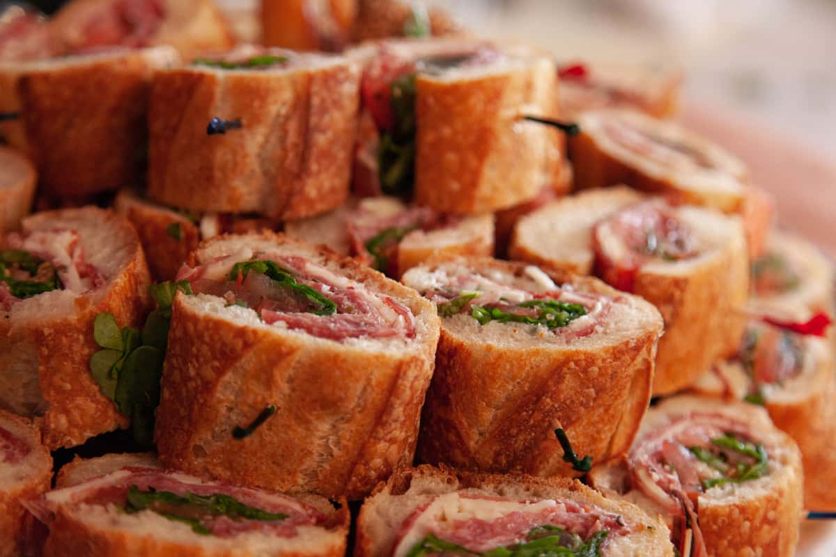Platter of delicious Italian sandwiches cut into bite-sized pieces, layered with salami, provolone, arugula, and nestled in crusty artisan bread, ideal for catering and party platters.