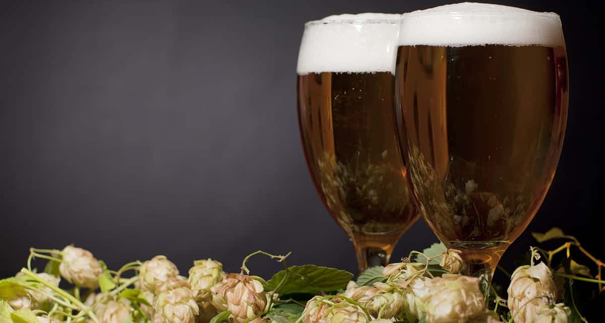 Two tall glasses of dark beer with thick, foamy heads served beside a plate of popcorn. The warm tones and rustic presentation create a cozy pub atmosphere, perfect for enjoying drinks and snacks with friends.