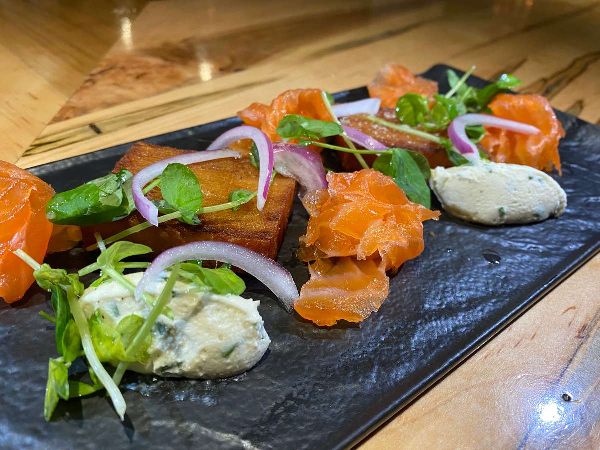 Colourful assorted sushi rolls arranged on a dark serving platter, featuring fresh fish, avocado, greens and vibrant garnishes.
