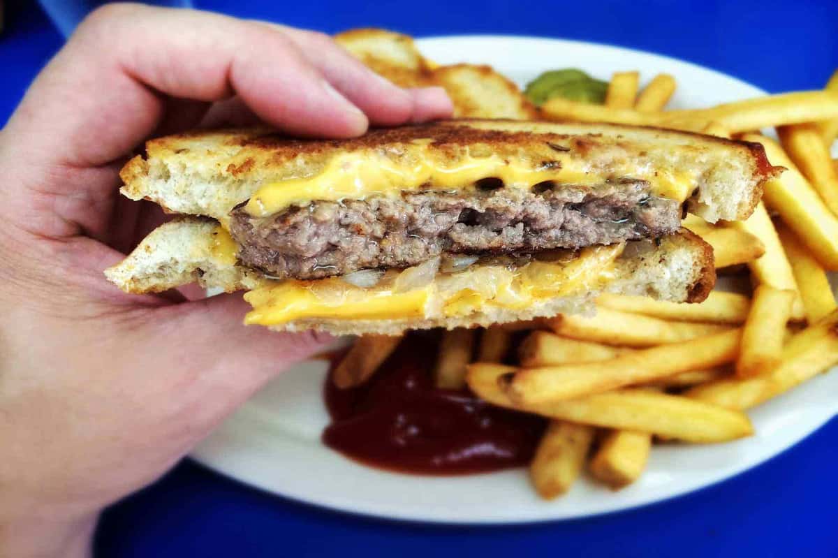 Cheeseburger patty melt sandwich on grilled bread with melted cheese, served with French fries and ketchup.