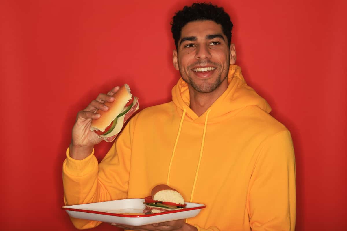 Man in yellow sweatshirt eating a sandwich