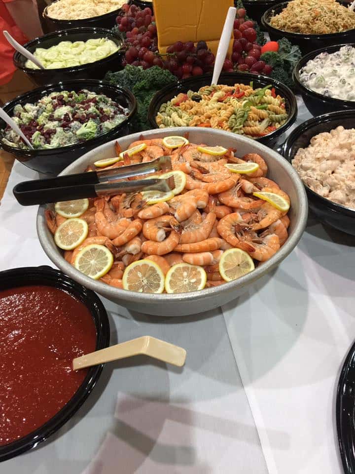 a bowl of shrimp and sliced lemons, a bowl of red soup another bowl of pasta, another with cucumber, rice, chicken on tablecloth