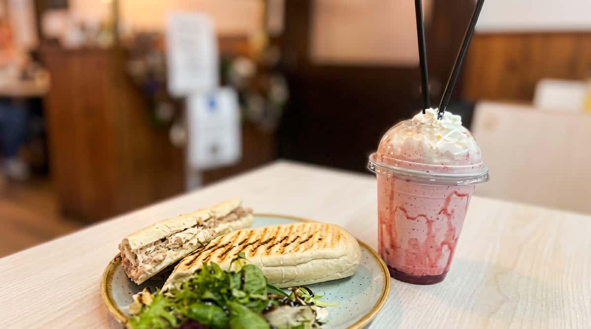 Panini sandwich with a side salad and a pink milkshake topped with whipped cream, on a table.