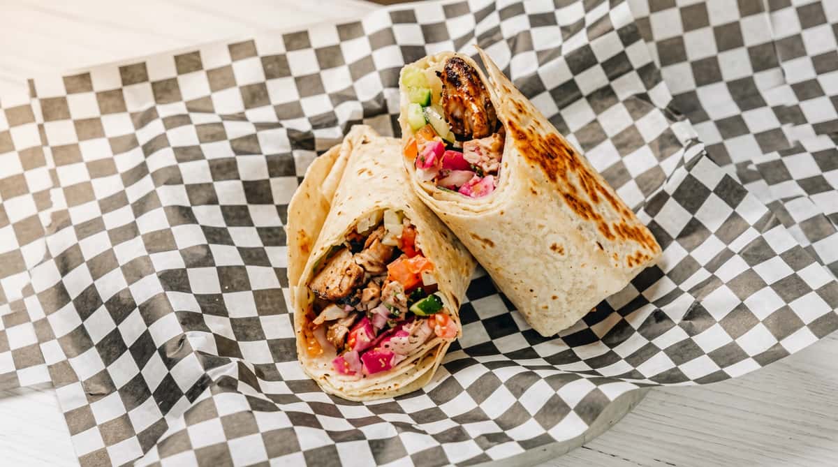 Two halves of a wrap filled with meat, red pickled onions, white sauce, and cucumber, served on checkered paper.