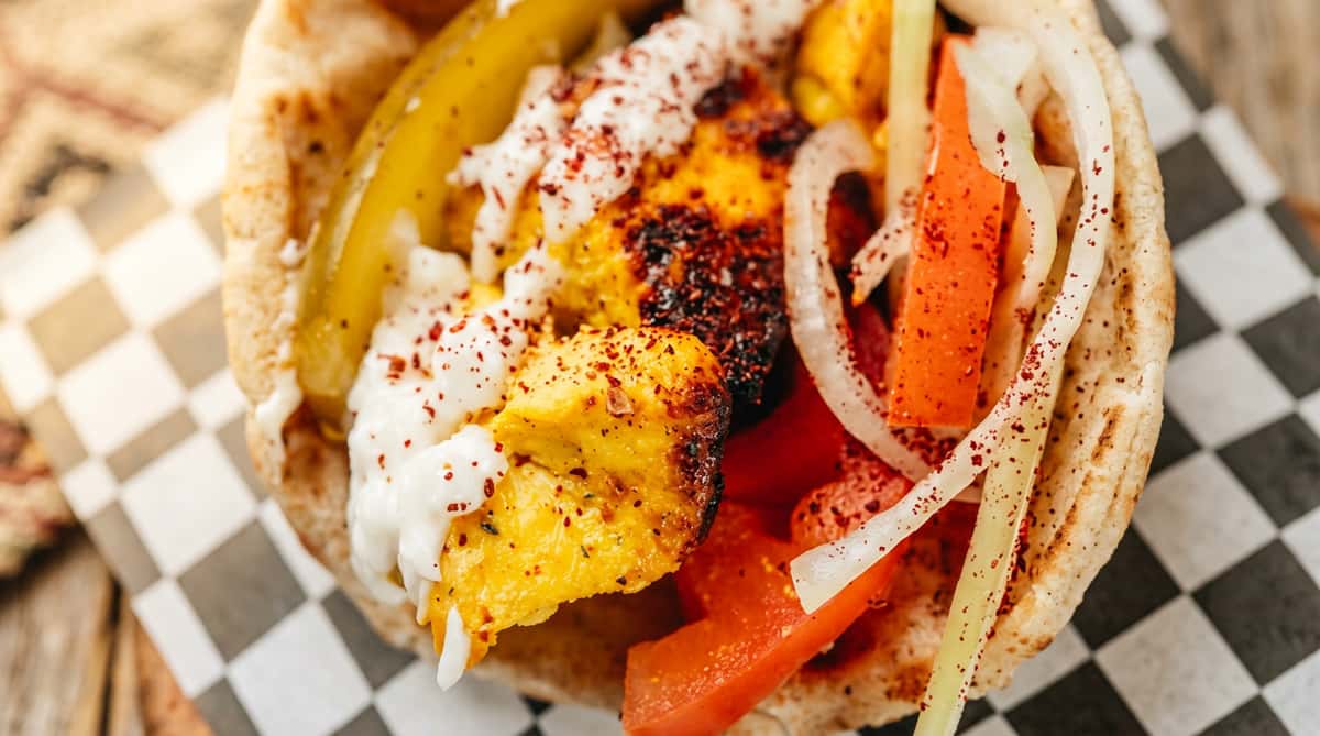 rilled chicken kebab or shawarma in pita with sauce, pickles, tomatoes, onions, and red spice.