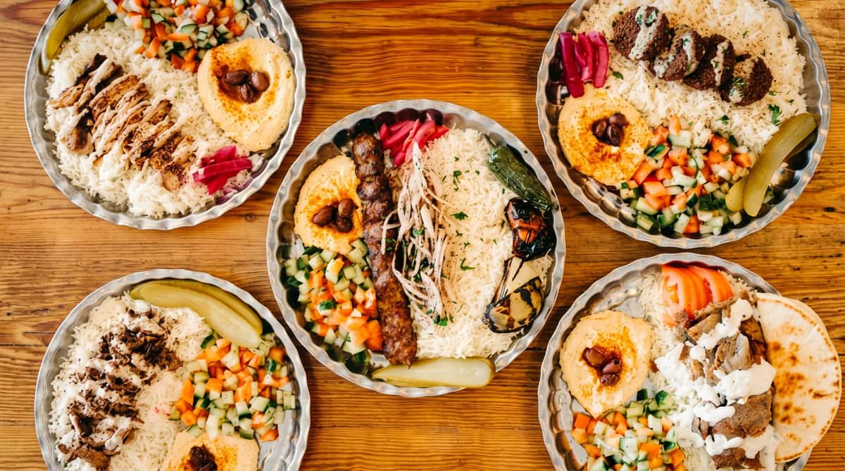 Assorted Middle Eastern plates with rice, hummus, falafel, kebab, and shawarma, along with salad and pickles.