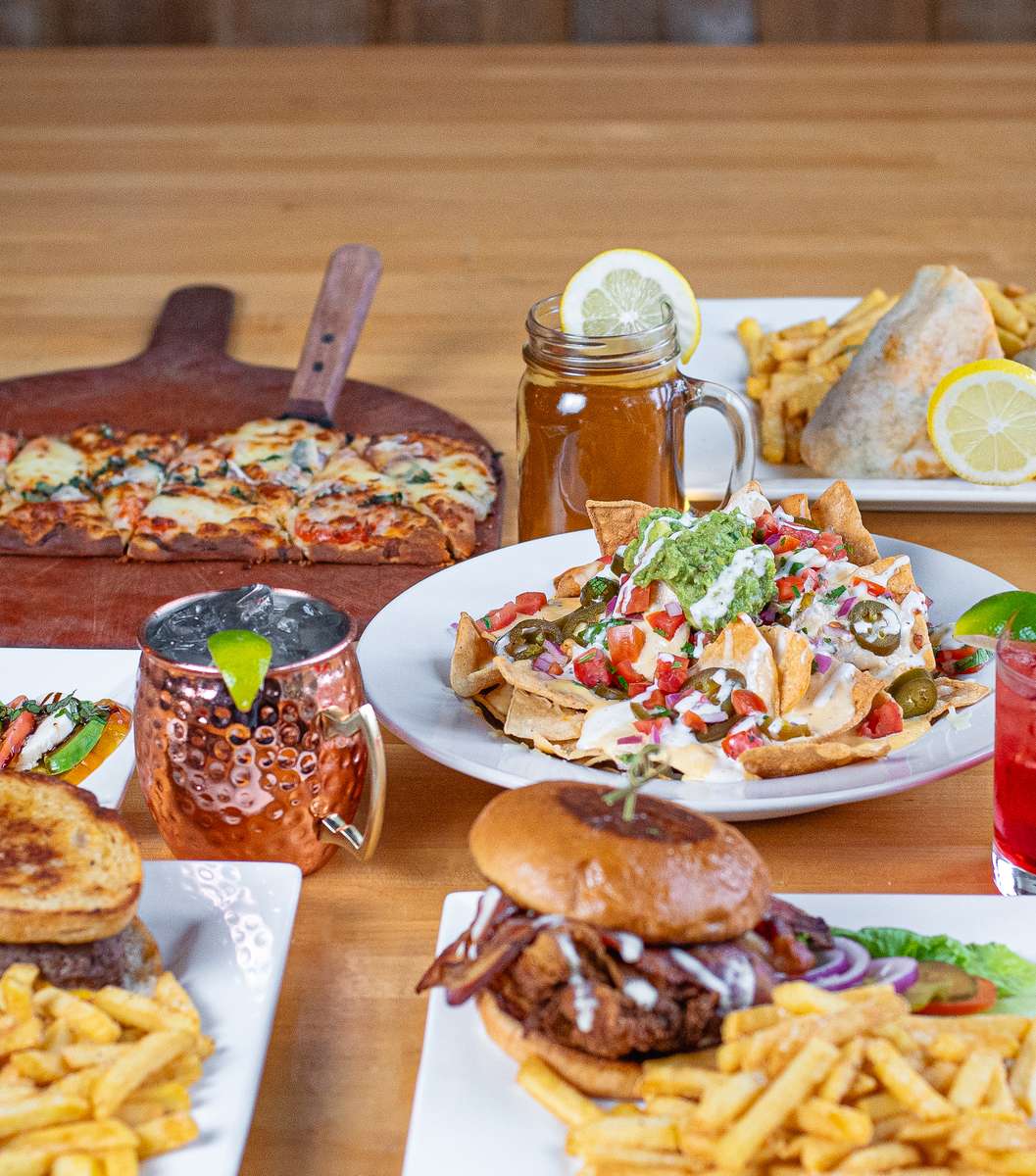 Table full of nachos, flatbread, sandwiches and drinks