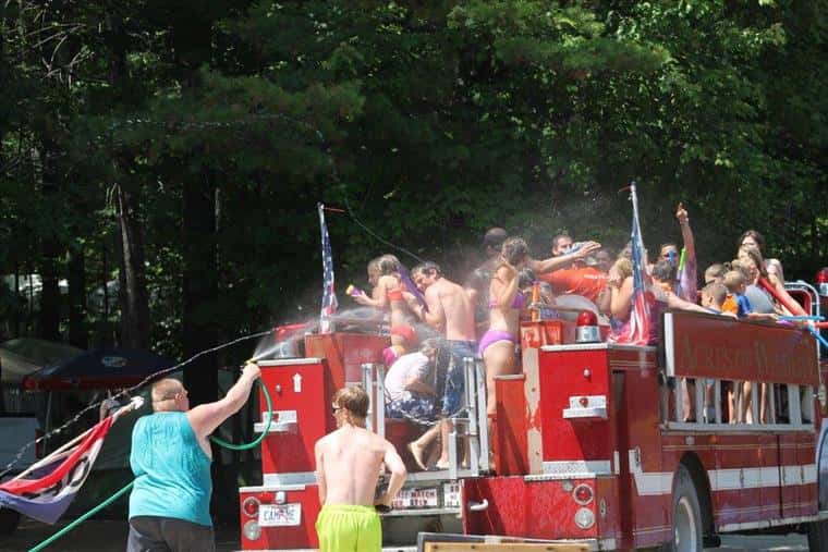 group of young kids on a fire truck having a large water gun fight