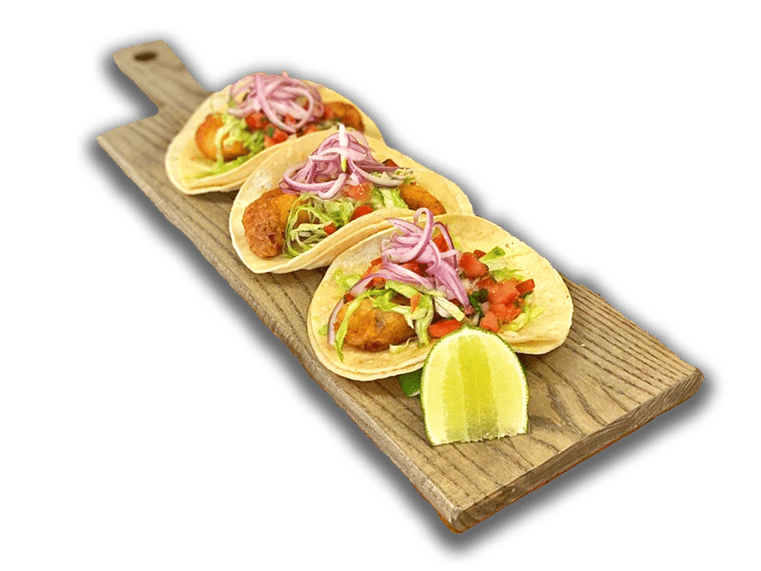 3 Fish tacos on a wooden board, topped with pickled onion, pico de gallo, and lettuce