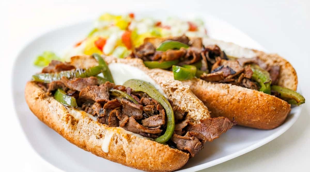 Philly cheesesteak sandwich with steak, green peppers, and melted cheese on a bun, with a side salad.
