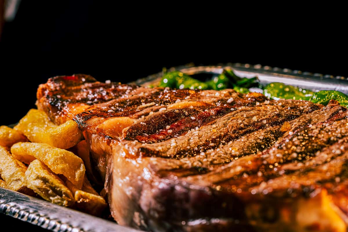 Close-up of a grilled steak with smoke rising, highlighting its juicy texture and grill marks.