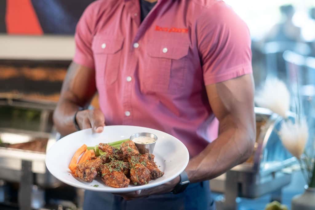 Image shows a man carrying out a plate of Asian Wings for a party.