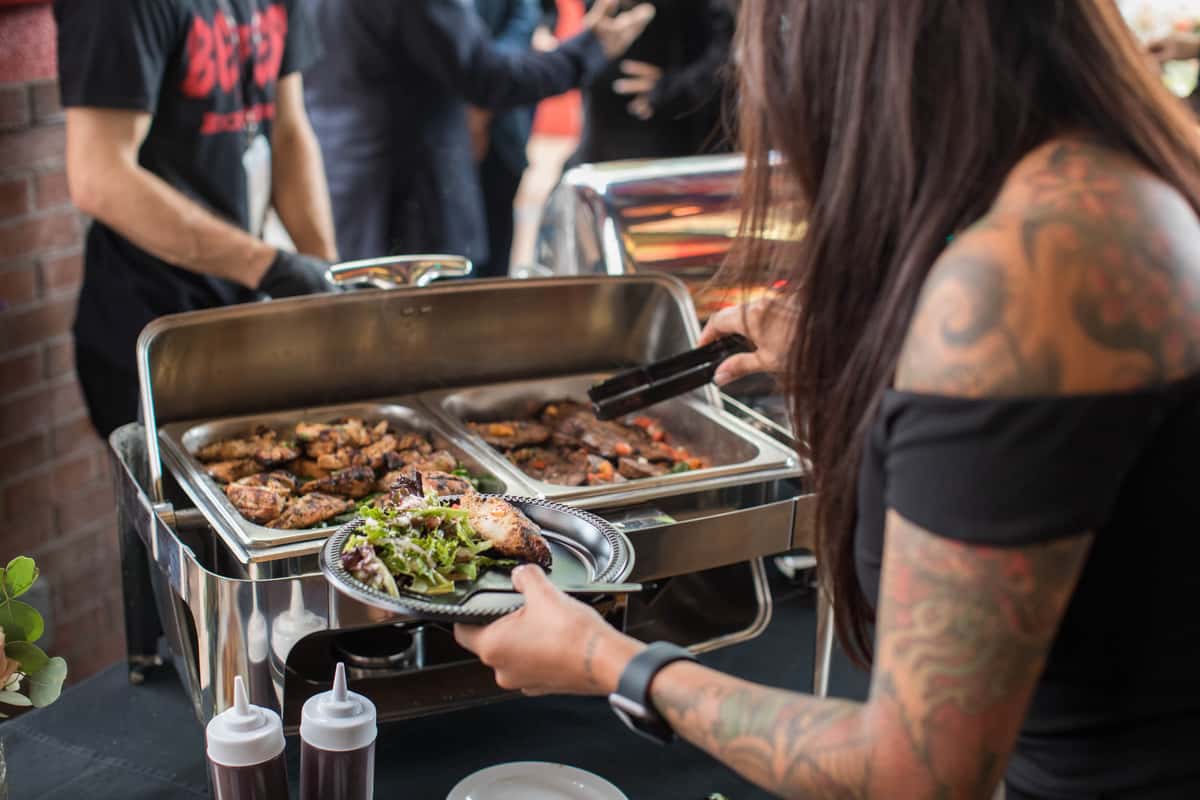 Image shows a woman getting food from a chafing dish on a buffet line at a private party at Rock & Brews.
