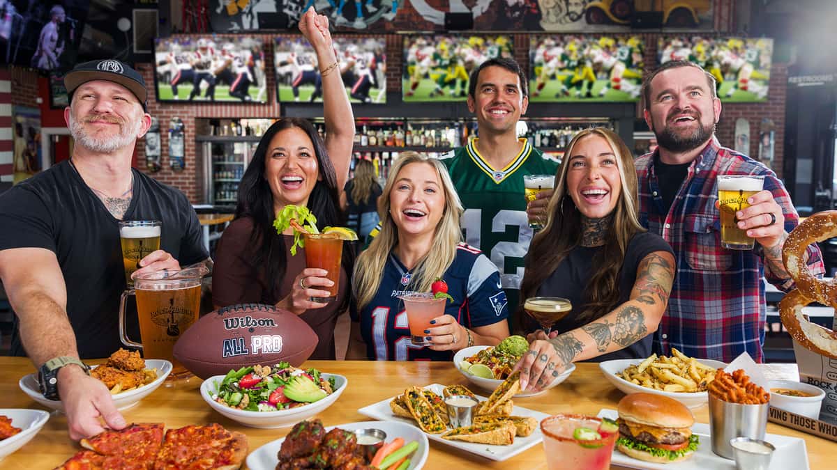 Group of friends raising glasses and giving high-fives while watching a sports game on TV at the bar in Grapevine, TX