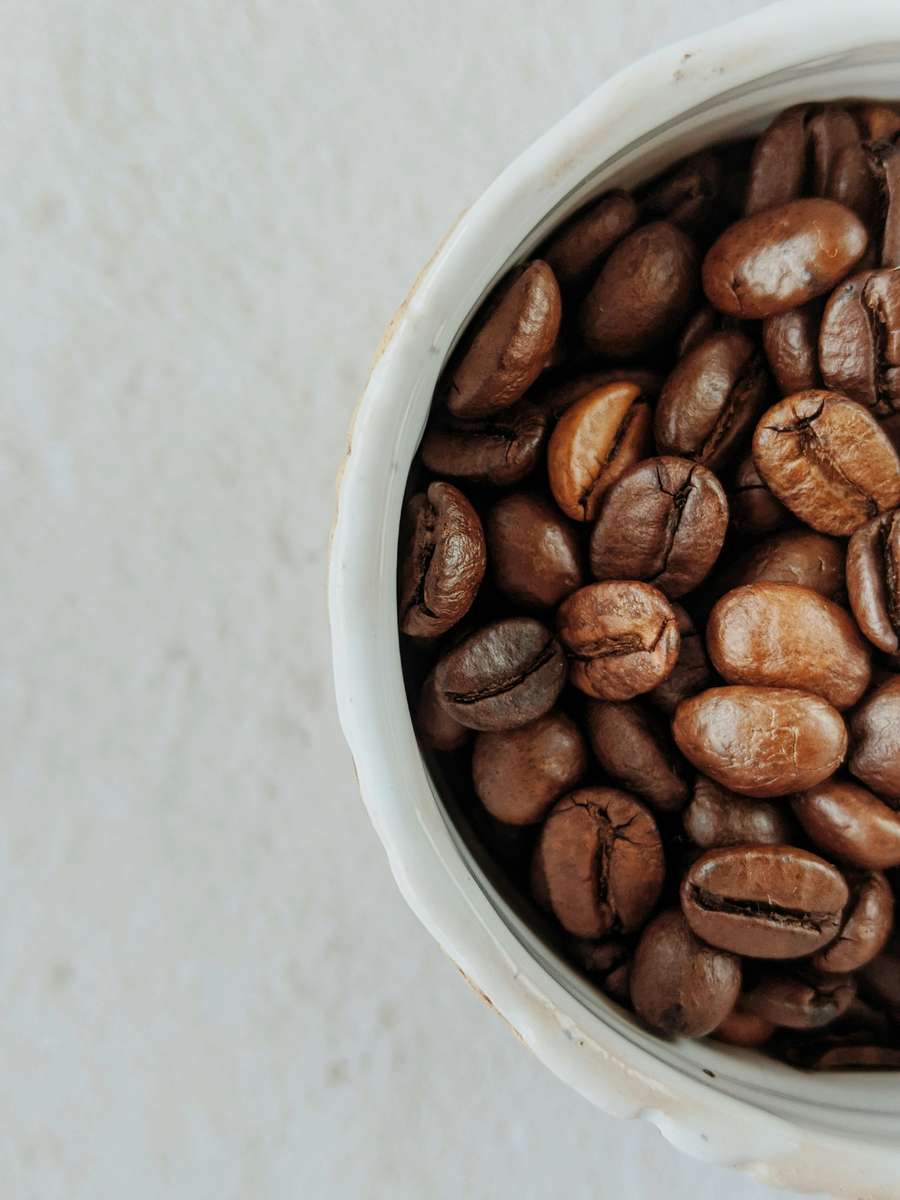 Close-up of glossy roasted coffee beans in a white ceramic bowl, emphasizing premium bean texture and color.