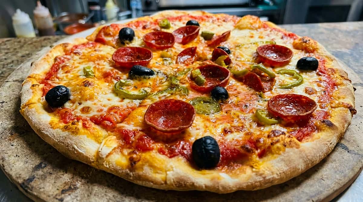 Pepperoni pizza topped with melted cheese, black olives, and green peppers on a white surface.
