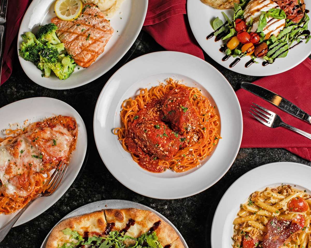 A table spread with a variety of Italian dishes including spaghetti and meatballs, grilled salmon and pizza