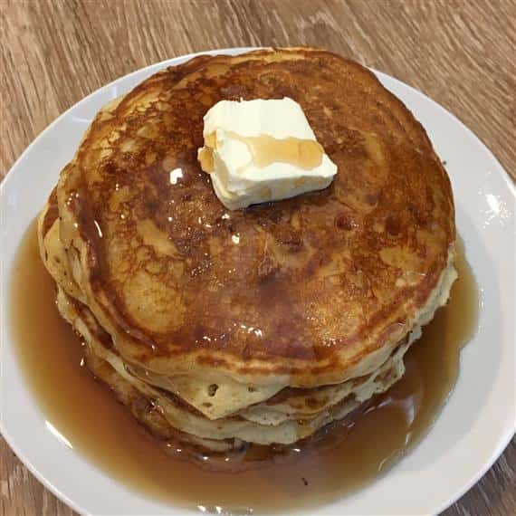 stack of pancakes covered in syrup topped with butter