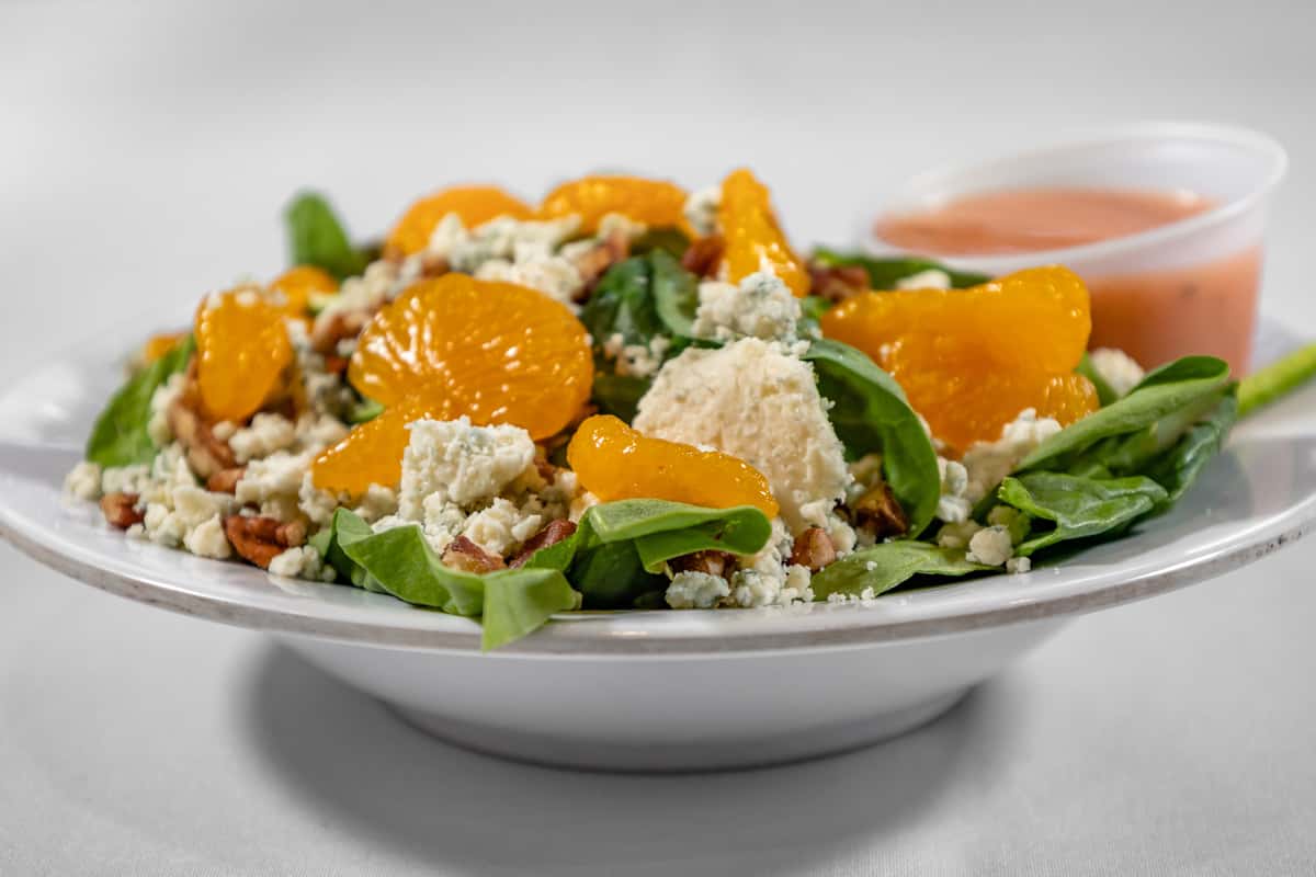 Fresh spinach salad topped with mandarin orange segments, crumbled blue cheese, candied pecans, and a scoop of chicken salad, served with a side of raspberry vinaigrette.